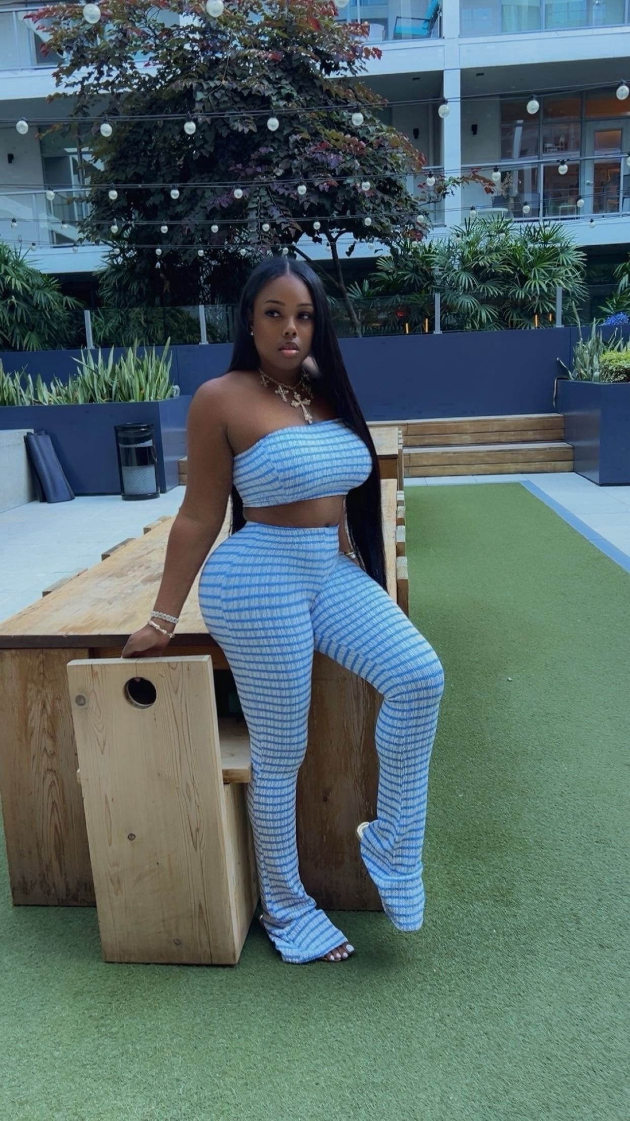 Woman in a blue outfit standing on a green surface with a wooden bench and plants in the background.