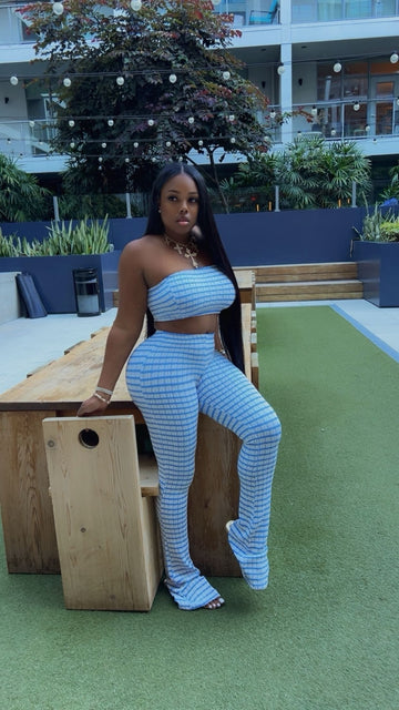 Woman in a blue outfit standing on a green surface with a wooden bench and plants in the background.